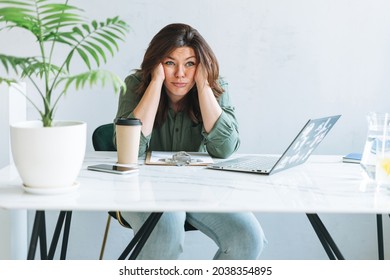 Young thinking unhappy brunette woman plus size working at laptop on table with house plant in bright modern office