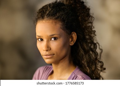 Young thoughtful Afro-american girl with long curly hair in her twenties turning to looking at the camera with a serious expression