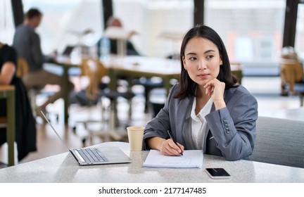 Young thoughtful Asian business woman executive manager wearing suit working in modern office, taking notes and thinking of professional plan, project management, considering new business ideas.