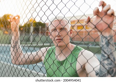 Young and thoughtful blond albino man leaning on a metal fence on the court - Powered by Shutterstock