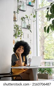 Young Thoughtful Dreamy Smiling African American Student Generation Z Girl With Afro Hair Sitting At Table With Laptop Thinking About Inspiration Ideas In Modern Cafe.