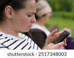 Young thoughtful girl looking at her phone screen sitting on a bench in the park. Concept of constant connection