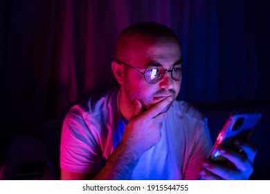 Young Thoughtful Man Looking At His Cellphone In Blue And Red Neon Light Room