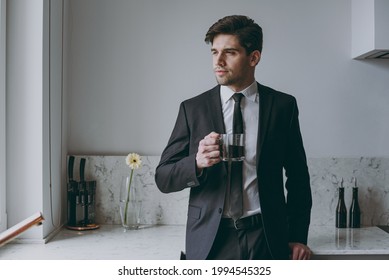 Young Thoughtful Minded Successful Employee Business Man Corporate Lawyer 20s In Formal Black Suit Shirt Tie Drink Coffee Breakfast Look Aside In Light Kitchen Achievement Career Lifestyle Concept.