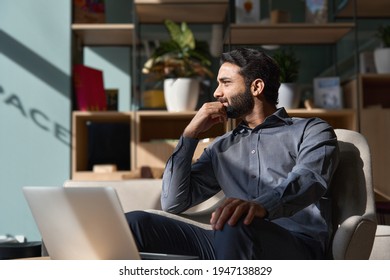 Young thoughtful smart indian professional business man executive looking away relaxing sitting on chair in modern office lobby with laptop, thinking of new ideas, dreaming of success, planning. - Powered by Shutterstock