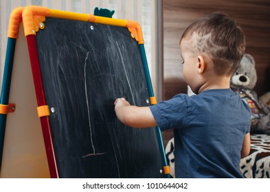 A Young Three Year Old Boy Drawing With Chalk On A Blackboard