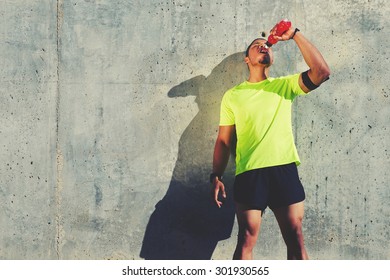 Young tired athlete refreshing with energy drink while standing against cement wall background with copy space area for your text message or content, male runner resting after exercise outdoors - Powered by Shutterstock