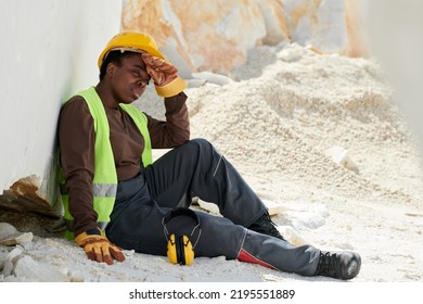 Young Tired Black Woman In Workwear Sitting On The Ground By Huge Marble Rock And Having Rest After Hard Work On Summer Day