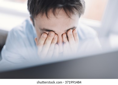 Young tired businessman rubbing his eye