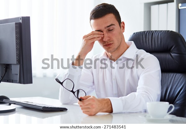 Young tired businessman\
rubbing his eye