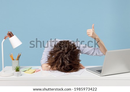 Young tired exhausted secretary employee business woman in shirt sit work sleep laid her head down on white office desk with pc laptop show thumb up gesture isolated on pastel blue background studio