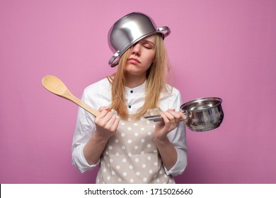 young tired girl cook in kitchen clothes with a pan on her head sleeps on a colored background, hard work of a housewife, lack of sleep