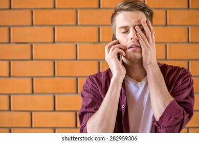 Young Tired Man Talking On Phone On Brick Wall Background.