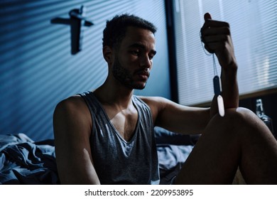 Young Tired And Sleepless Man With PTSD Looking At Metallic Medallion On Silver Chain While Holding It In Front Of His Face