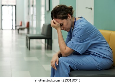 Young tired or stressed female doctor in uniform sitting in hospital corridor with her head in hands after shocking news - Powered by Shutterstock