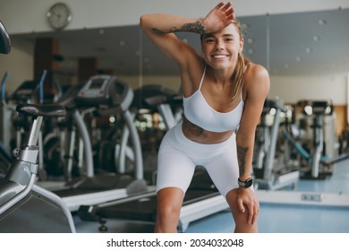 Young tired strong skinny sporty athletic sportswoman woman in white sportswear warm up training near treadmill stand leaning on knees put hand on head in gym indoor Workout sport motivation concept - Powered by Shutterstock