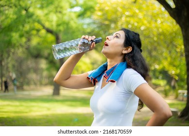 Young Tired Thirsty Indian Woman Athlete Takes A Break Drinking Water With Bottle, Asian Female Out On A Run On A Hot Day In The Park.