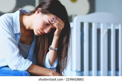 Young Tired Woman Sitting On The Bed Near Children's Cot. Young Mom.