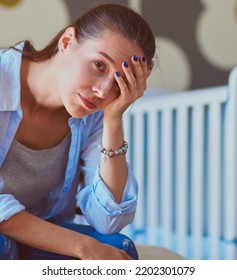 Young Tired Woman Sitting On The Bed Near Children's Cot. Young Mom.