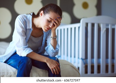 Young tired woman sitting on the bed near childrens cot