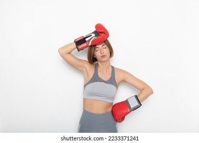 Young tired woman in sportswear and boxing gloves standing isolated on white background. Exhausted Female boxer posing close to white wall - Powered by Shutterstock