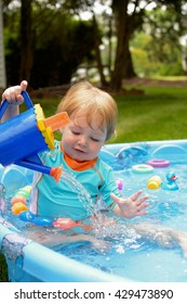 Young Toddler Boy Playing In Kiddie Pool With Watering Can