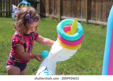 Young Toddler Girl In Summer Time Playing Outside Focusing On Hand Eye Coordination And Fine Motor Skills With Water Toys.