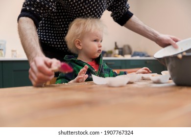 A Young Toddler Having Fun Helping His Dad Bake Cakes In The Kitchen.