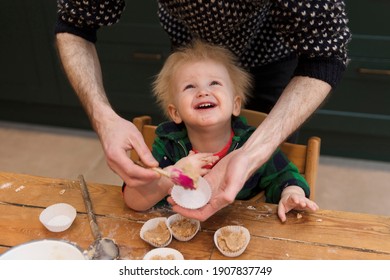 A Young Toddler Having Fun Helping His Dad Bake Cakes In The Kitchen.