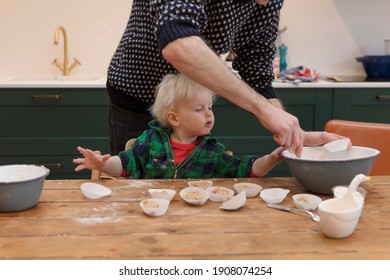 A Young Toddler Having Fun Helping His Dad Bake Cakes In The Kitchen.