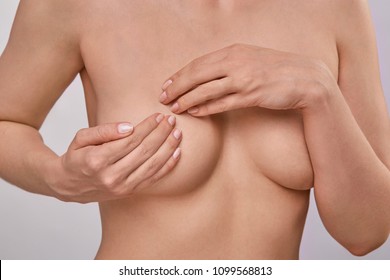 Young topless woman doing breast self-exam (BSE). Checking up breast changes, possible lumps, distortions or swelling.  Breast cancer awareness. 