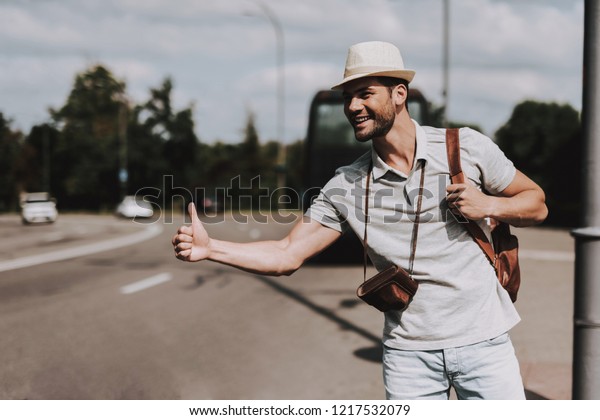 Young Tourist with Backpack Hitchhiking on Road.\
Casually dressed Handsome Man with Camera on Neck trying to Catch\
Car on Highway. Tourism and People Concept. Active Lifestyle.\
Summer Vacation