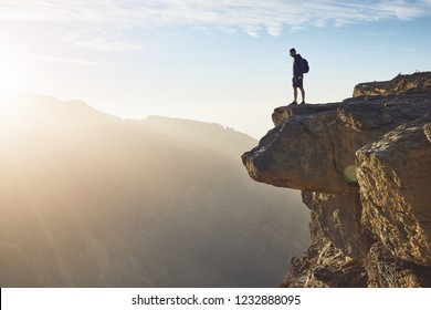 Young tourist with backpack standing on the edge of cliff at sunrise. Jebel Akhdar, Grand Canyon of Oman.   - Powered by Shutterstock