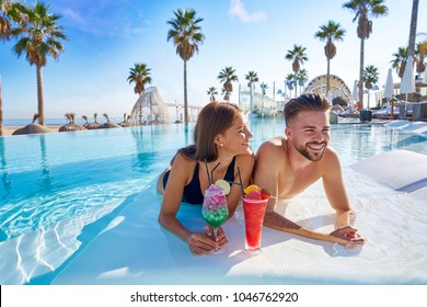 Young tourist couple on infinity pool drinking cocktails at resort on the beach - Powered by Shutterstock