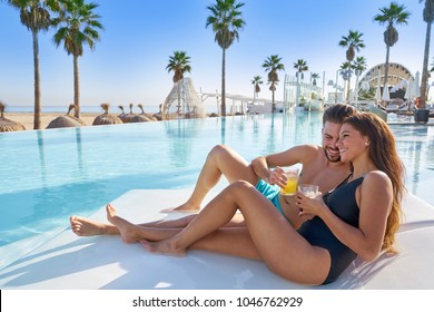 Young Tourist Couple On Infinity Pool Hammock At Resort On The Beach Drinking Soda