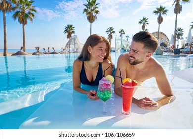 Young tourist couple on infinity pool drinking cocktails at resort on the beach - Powered by Shutterstock