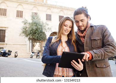 Young tourist couple standing together in a destination city holding and sharing a digital tablet pad while on vacation, smiling. - Powered by Shutterstock