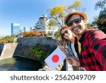 A young tourist couple taking a selfie with Japan flag at Osaka Castle, Osaka Castle is one of the most famous landmarks in Japan and Osaka, vacation lifestyle.