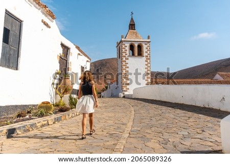 A young tourist girl walking next to the white church of Betancuria, west coast of the island of Fuerteventura, Canary Islands. Spain