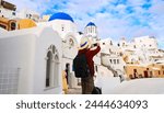 Young tourist man backpack using smartphone take picture at View of blue church dome in Oia village,Santorini,Greece