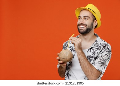 Young tourist man in beach shirt hat hold cocktail juice in coconut bowl with straw look aside on workspace isolated on plain orange background studio portrait Summer vacation sea rest sun tan concept