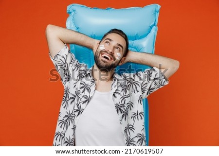 Young tourist man with spf sunscreen cream on wear beach shirt lies on blue inflatable mattress hotel pool look overhead isolated on plain orange background. Summer vacation sea rest sun tan concept