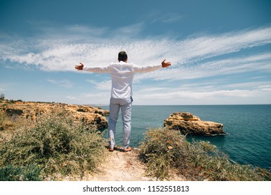 Young tourist man standing on the edge of reef enjoying ocean or sea view of turquoise water with raised hands