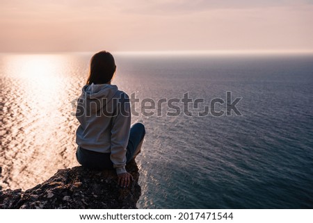 A young tourist Woman enjoying sunset over sea mountain landscape while sitting outdoor. Women's yoga fitness routine. Healthy lifestyle, harmony and meditation