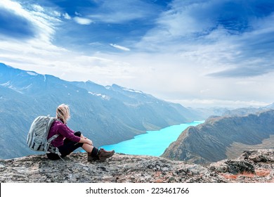 Young tourist woman is feeling free and sitting on the top of the mounting and looking at a beautiful landscape