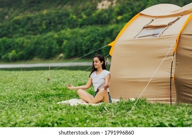 Young tourist woman sits near a tent and meditating.  Morning meditation. Young woman resting near camping tent in the nature near the river and mountain. - Shutterstock ID 1791996860