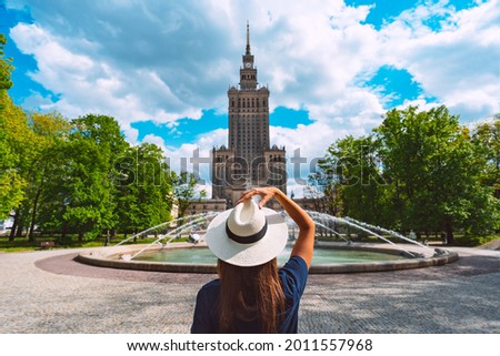 Young tourist woman in white sun hat walking in the park near Palace of Culture and Science in Warsaw city, Poland. Summer vacation in Warsaw