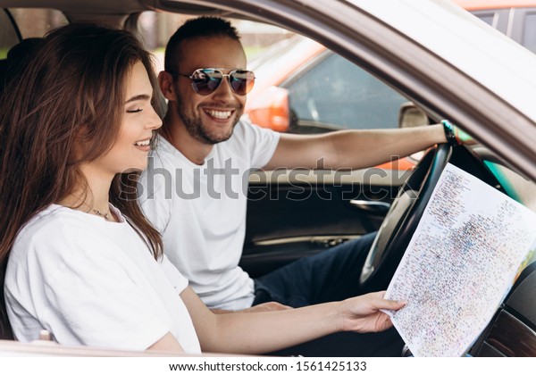 Young tourists couple handsome man and beautiful\
woman travelling on vacation by car trying to find hotel looking in\
the map holiday mood.