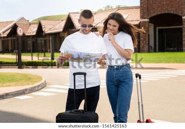 Young tourists couple handsome man and\
beautiful woman can not find way to hotel standing on the street\
with baggage checking the map looking\
excited.