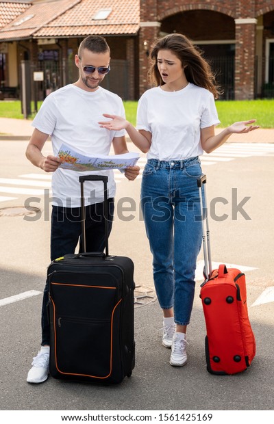 Young tourists couple handsome man and\
beautiful woman can not find way to hotel standing on the street\
with baggage checking the map looking lost\
.